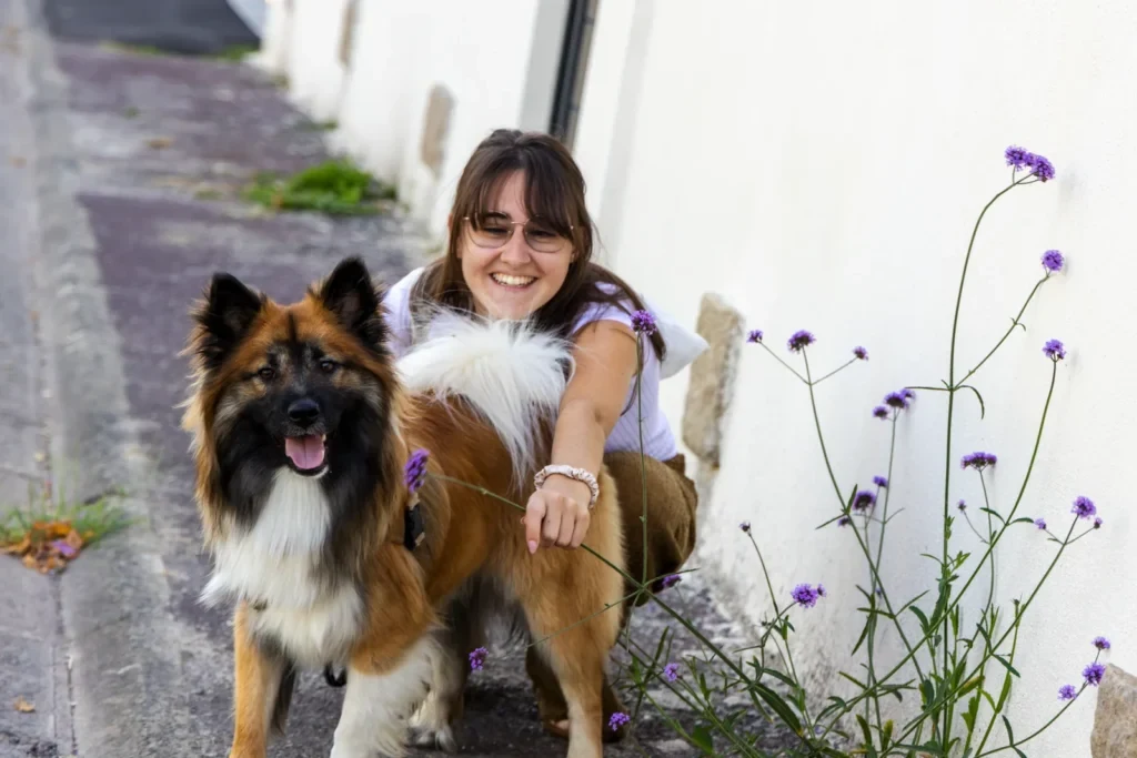 Jeune femme accroupie près de son chien dans une ruelle fleurie